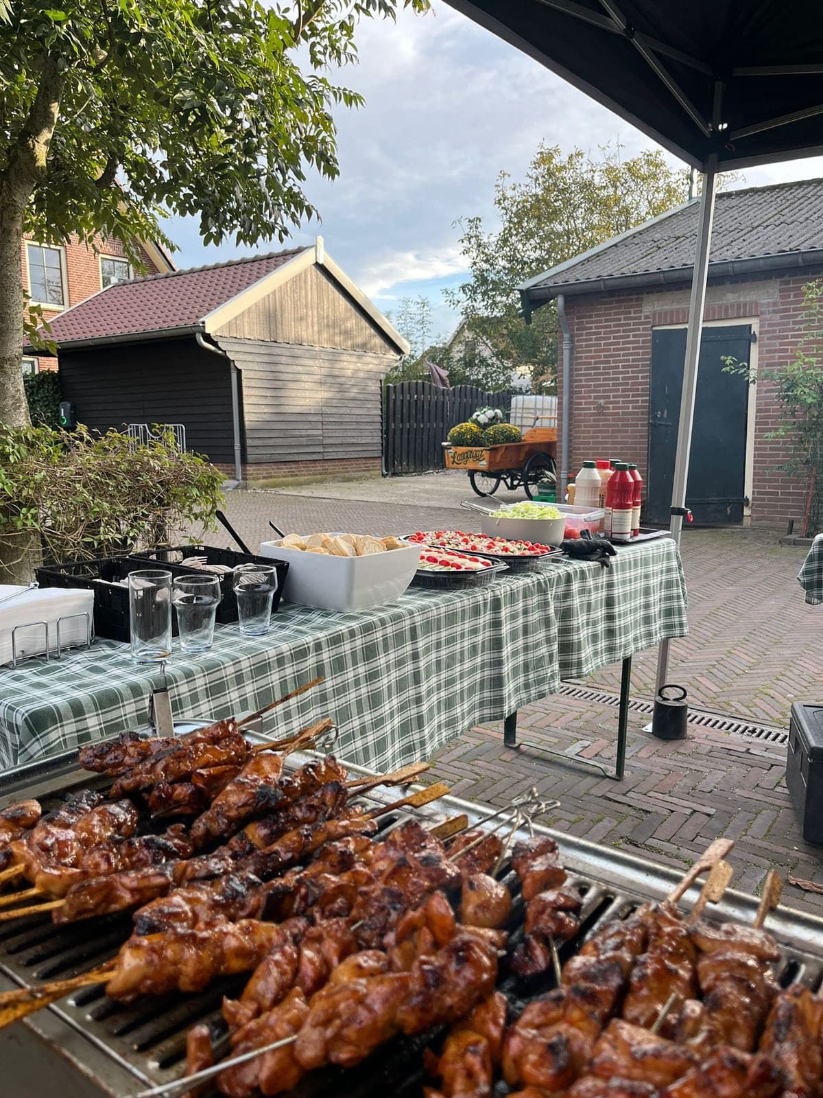 Saté op de barbecue met op de achtergrond een gedekte buffettafel met stokbrood en salades