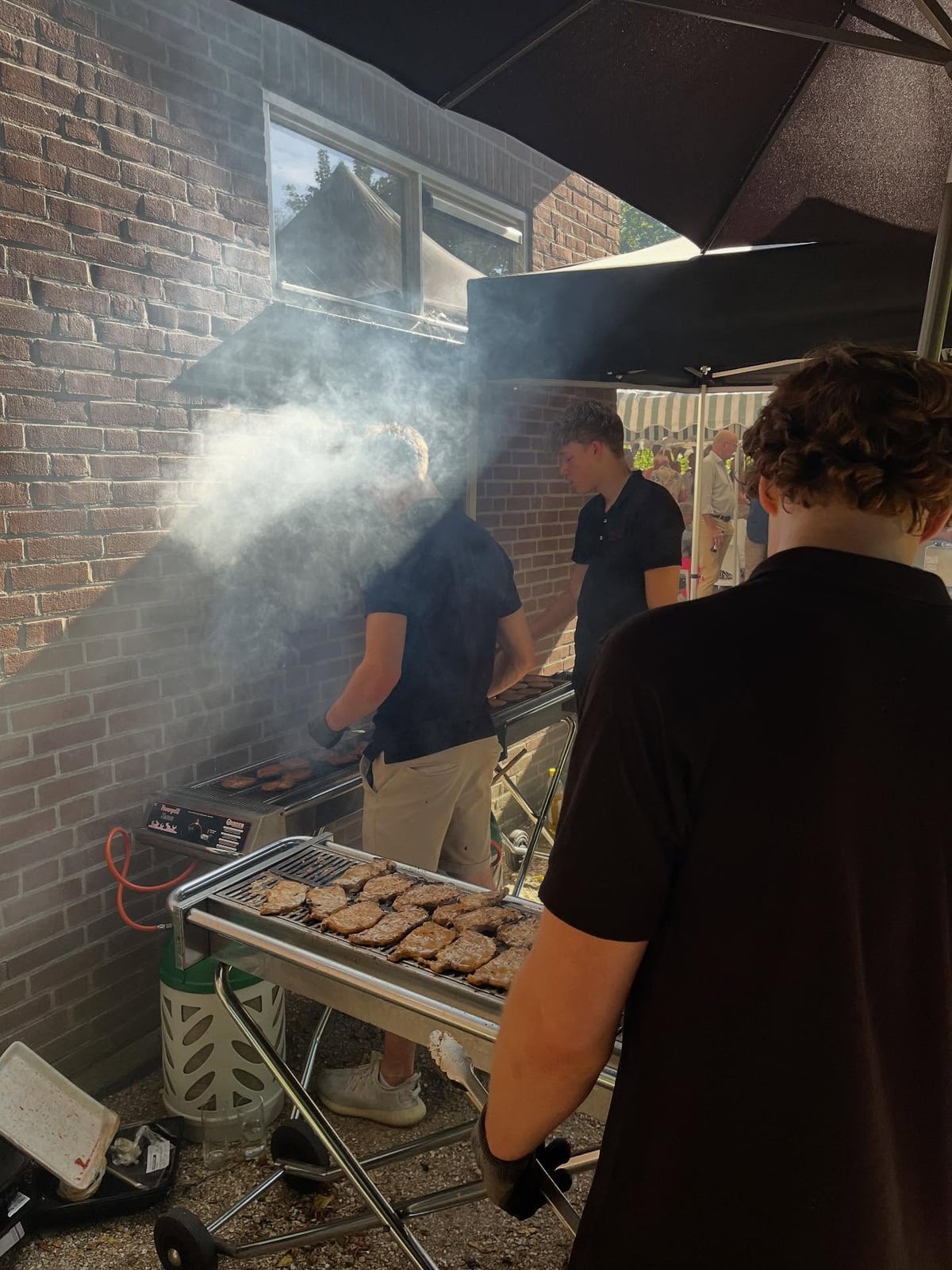Medewerkers van Vuur en Vlam aan de rokende grill naast een bakstenen muur
