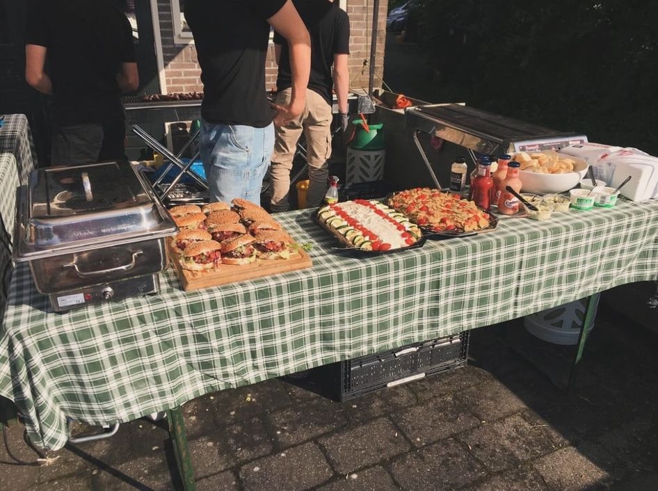 Buffettafel met een gingham tafelkleed, een plank met hamburgers, salades en sauzen
